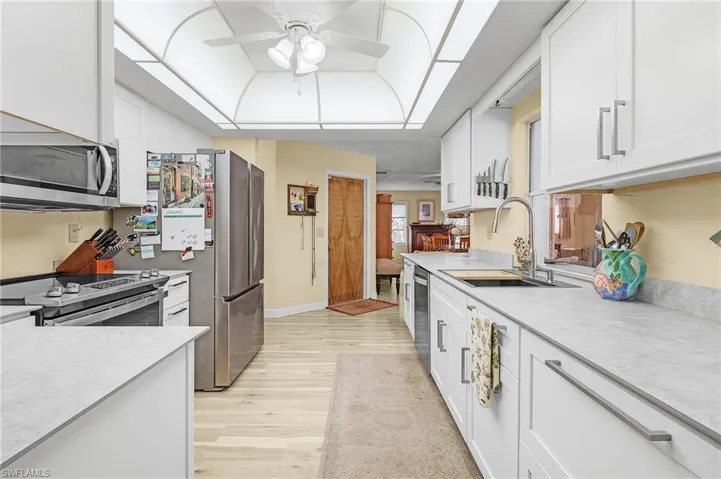 Kitchen with white cabinets, stainless steel appliances, sink, light wood-type flooring, and ceiling fan