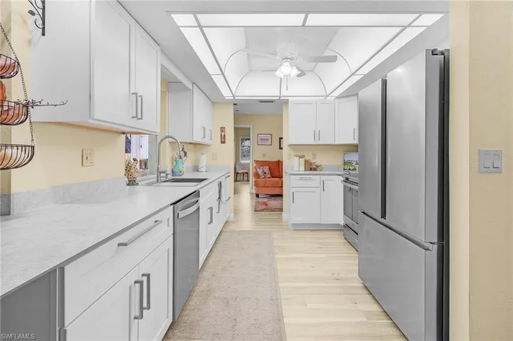 Kitchen with light hardwood / wood-style floors, appliances with stainless steel finishes, white cabinets, sink, and ceiling fan