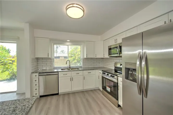 Kitchen with sink, white cabinetry, light wood-type flooring, and stainless steel appliances