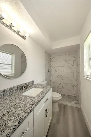 Bathroom featuring wood-type flooring, toilet, vanity, and a tile shower