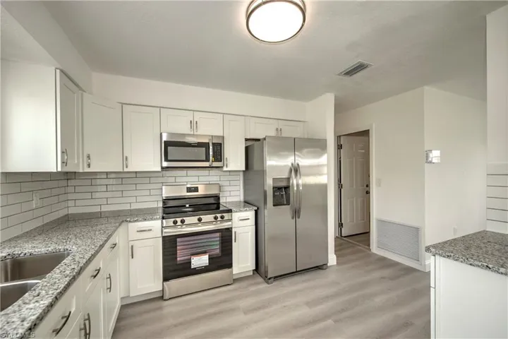 Kitchen with light hardwood / wood-style flooring, tasteful backsplash, white cabinets, and stainless steel appliances
