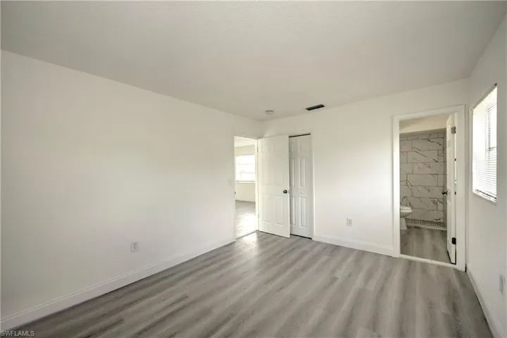 Unfurnished bedroom with a closet, ensuite bathroom, and wood-type flooring