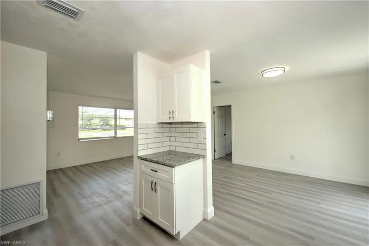 Kitchen with decorative backsplash, light wood-type flooring, light stone counters, and white cabinetry