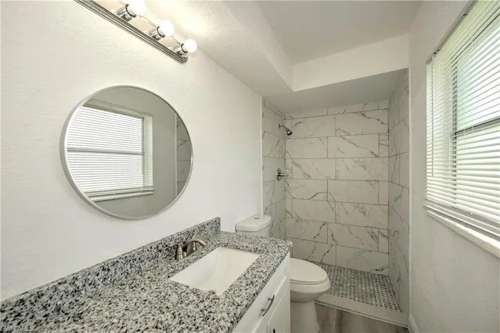 Bathroom featuring vanity, tiled shower, toilet, and hardwood / wood-style floors