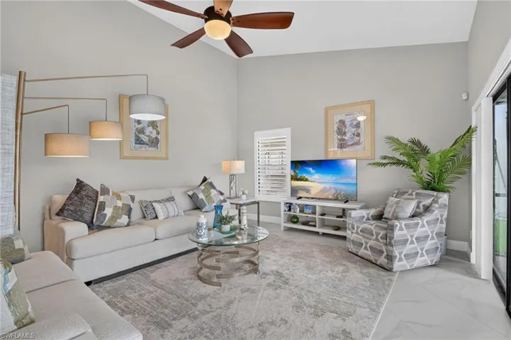 Bright living area featuring vaulted ceilings, a ceiling fan with integrated lighting, and large format tile flooring