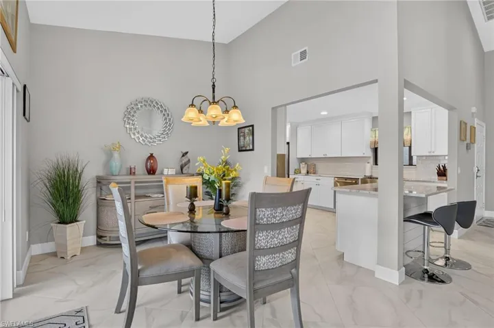 Vaulted ceiling dining area featuring a glass-top table, chandelier, and tile flooring