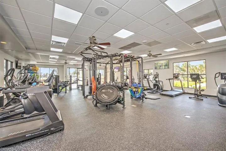 Fitness center featuring rubberized flooring, abundant natural light from multiple windows, ceiling-mounted light panels, and ceiling fans