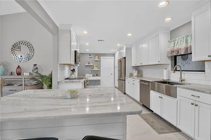 Kitchen featuring a large central island with a stone countertop, white shaker-style cabinetry, and integrated stainless steel appliances
