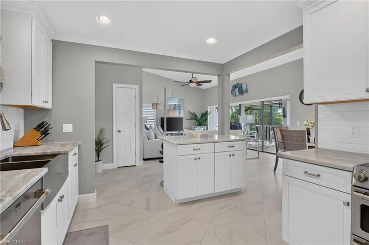 Open-concept kitchen featuring an island, white shaker cabinetry, light-toned countertops, tile flooring, and stainless steel appliances