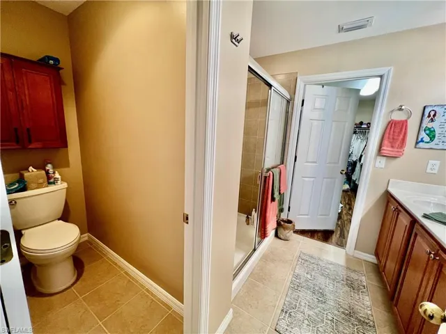 Bathroom with a walk in closet, toilet, baseboards, a stall shower.