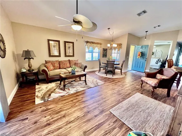 Living room featuring ceiling fan with notable chandelier, visible vents, wood finished floors, and baseboards