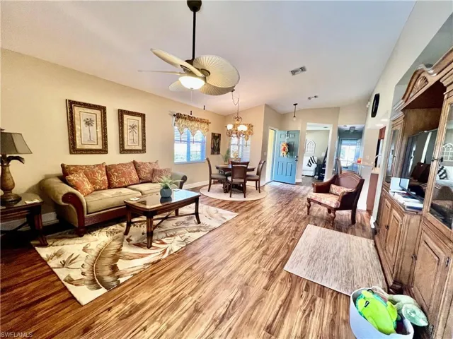 Living area with light wood-style flooring, ceiling fan with notable chandelier, lofted ceiling, and a wealth of natural light