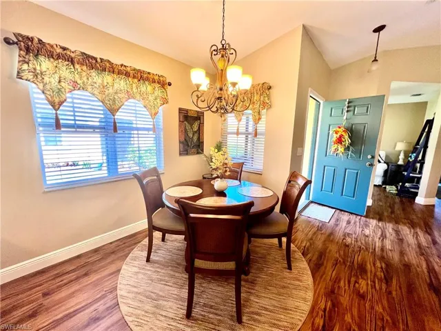 Dining room with a chandelier, baseboards, vaulted ceiling, and wood finished floors