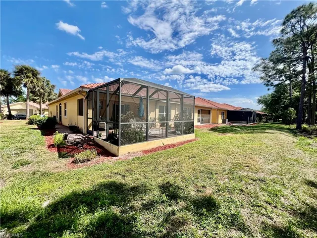 Back of house featuring a lawn, a tile roof, stucco siding, and a lanai