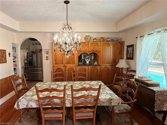 Dining area with arched walkways, hanging lights, dark wood-type flooring, wooden walls, and wainscoting