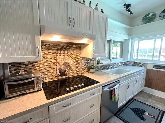Kitchen with dishwasher, black electric stovetop, decorative backsplash, white cabinets, and track lighting