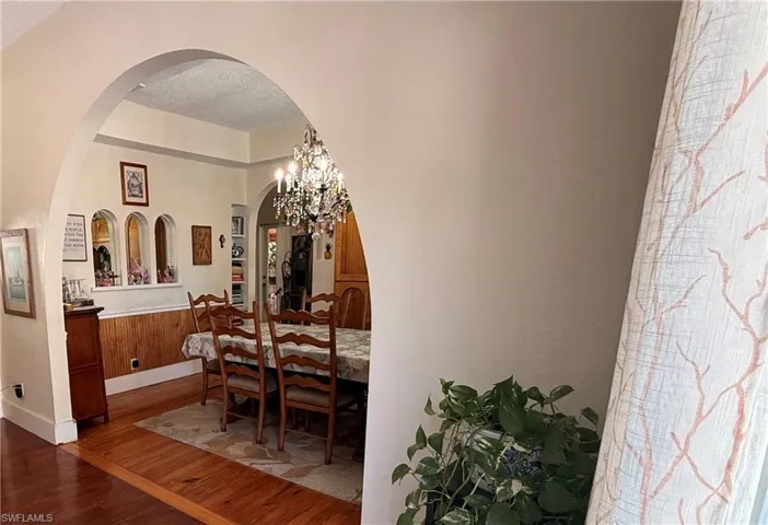 Dining room with wood finished floors, suspended lighting, arched walkways, and a textured ceiling