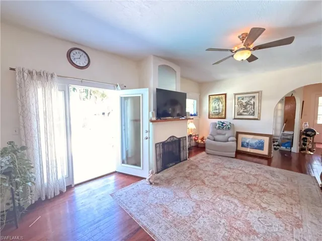 Living room featuring arched walkways, dark wood-style flooring, ceiling fan, and a fireplace