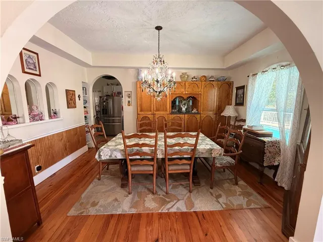 Dining room featuring arched walkways, light wood-style flooring, hanging lights, a textured ceiling, and a wainscoted wall