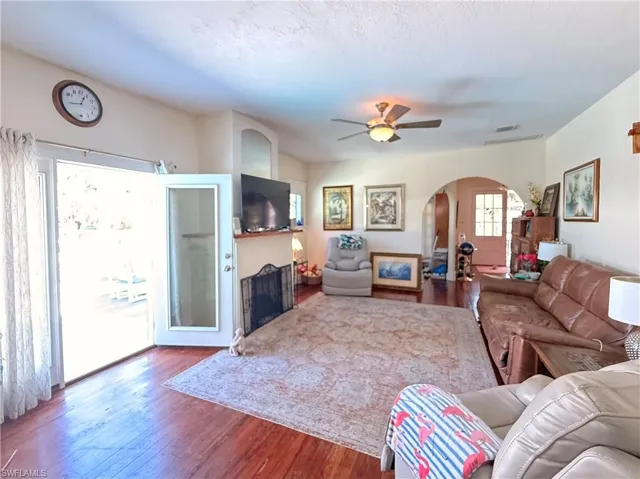 Living area featuring dark wood-type flooring, ceiling fan, arched walkways, and a fireplace