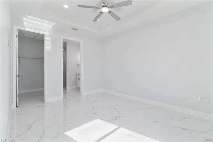 Unfurnished bedroom featuring a spacious closet, recessed lighting, light marble finish floors, connected bathroom, and a ceiling fan
