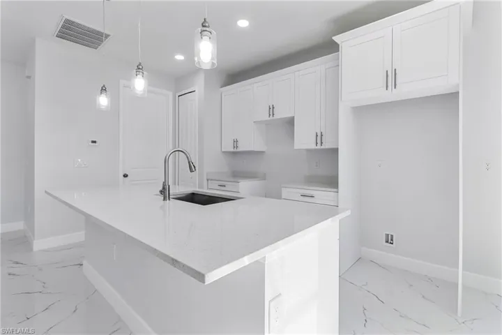 Kitchen featuring light stone countertops, white cabinets, a kitchen island with sink, pendant lighting, and recessed lighting
