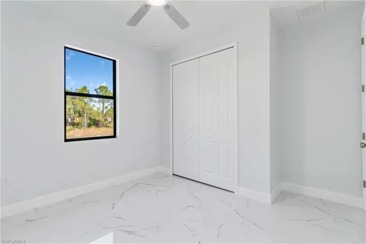 Unfurnished bedroom featuring light marble finish floors, ceiling fan, and a closet