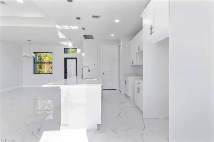 Kitchen featuring white cabinets, a kitchen island with sink, recessed lighting, pendant lighting, and light marble finish flooring