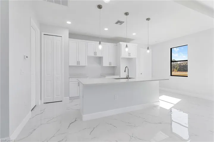 Kitchen with white cabinetry, a center island with sink, recessed lighting, light stone countertops, and hanging light fixtures