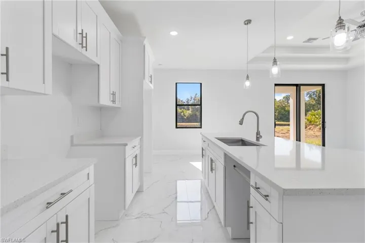 Kitchen featuring white cabinets, light stone counters, recessed lighting, a raised ceiling, and healthy amount of natural light