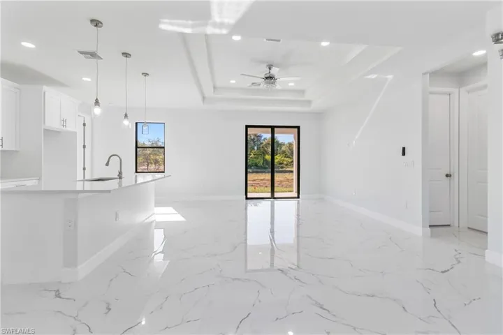 Unfurnished living room featuring recessed lighting, a ceiling fan, a raised ceiling, and light marble finish flooring