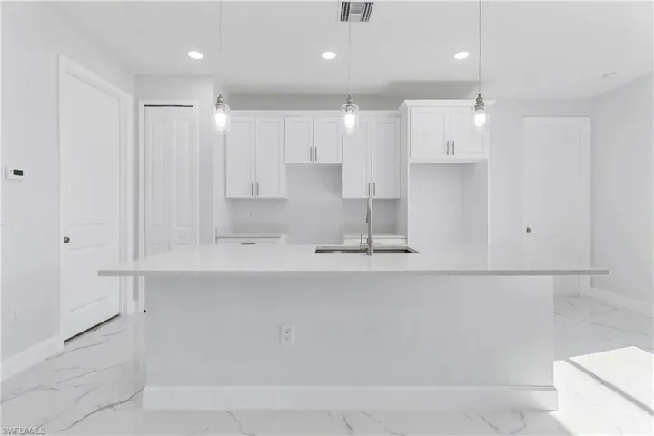 Kitchen featuring light stone countertops, recessed lighting, white cabinets, pendant lighting, and light marble finish flooring