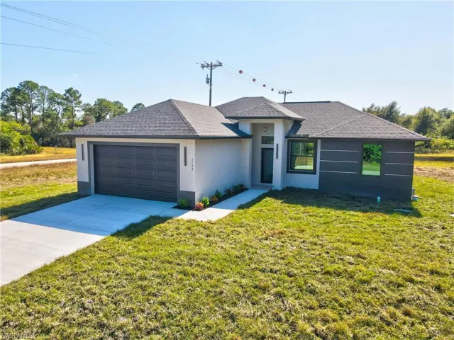 View of front of property with roof with shingles, stucco siding, concrete driveway, a garage, and a front lawn
