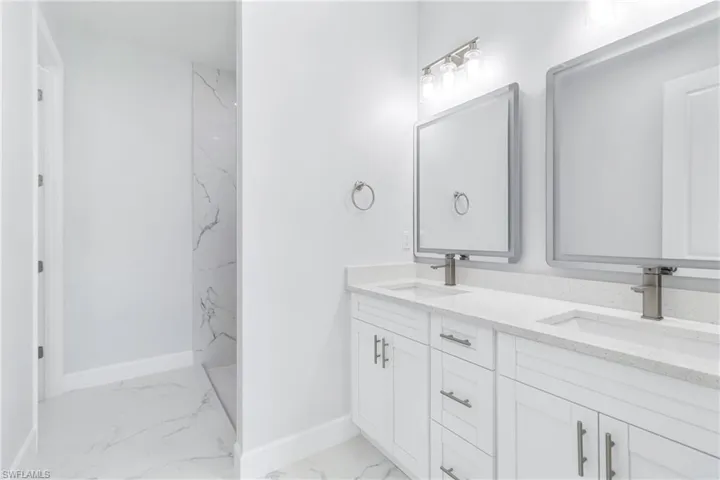 Bathroom featuring double vanity, light marble finish floors, and a marble finish shower