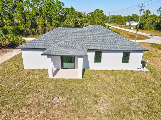 Rear view of property with stucco siding, roof with shingles, and a lawn