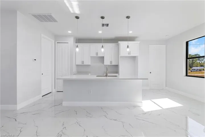 Kitchen featuring white cabinetry, recessed lighting, a center island with sink, light stone counters, and pendant lighting
