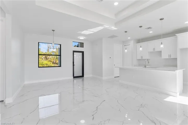 Unfurnished living room featuring a chandelier, a raised ceiling, light marble finish flooring, and recessed lighting