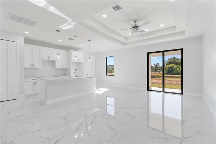 Unfurnished living room with recessed lighting, light marble finish floors, a ceiling fan, and a raised ceiling