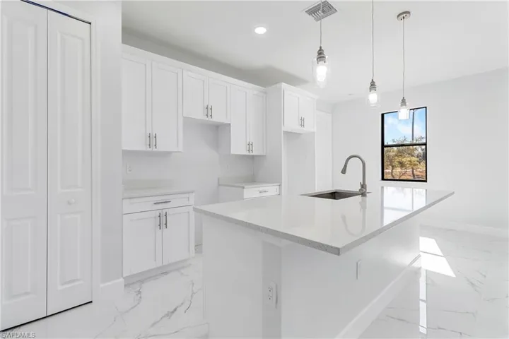 Kitchen with light marble finish floors, light stone countertops, white cabinets, a kitchen island with sink, and recessed lighting