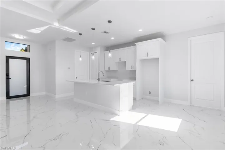 Kitchen featuring white cabinets, a kitchen island with sink, decorative light fixtures, light stone counters, and light marble finish flooring