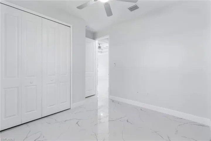 Unfurnished bedroom featuring light marble finish flooring, a closet, and a ceiling fan