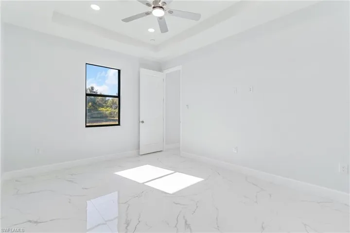 Unfurnished room featuring a tray ceiling, light marble finish floors, and recessed lighting