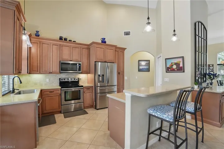 Kitchen featuring appliances with stainless steel finishes, a sink, light countertops, decorative backsplash, and a high ceiling