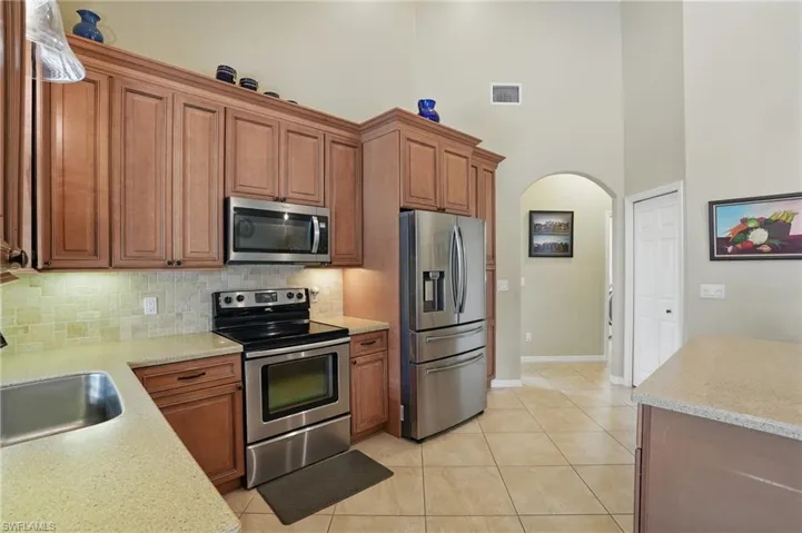 Kitchen with stainless steel appliances, a high ceiling, arched walkways, decorative backsplash, and brown cabinetry