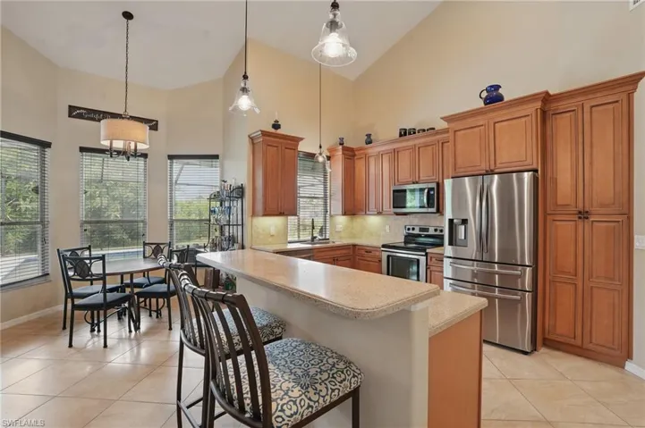 Kitchen with appliances with stainless steel finishes, high vaulted ceiling, light countertops, baseboards, and light tile patterned floors