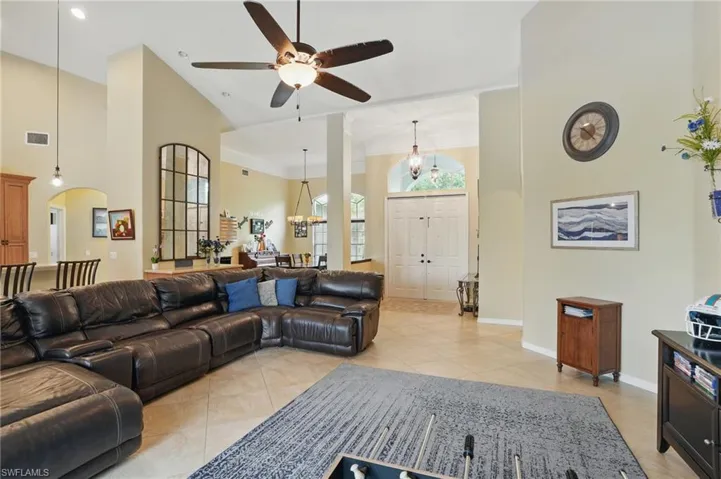 Living room with high vaulted ceiling, light tile patterned flooring, ceiling fan, baseboards, and arched walkways