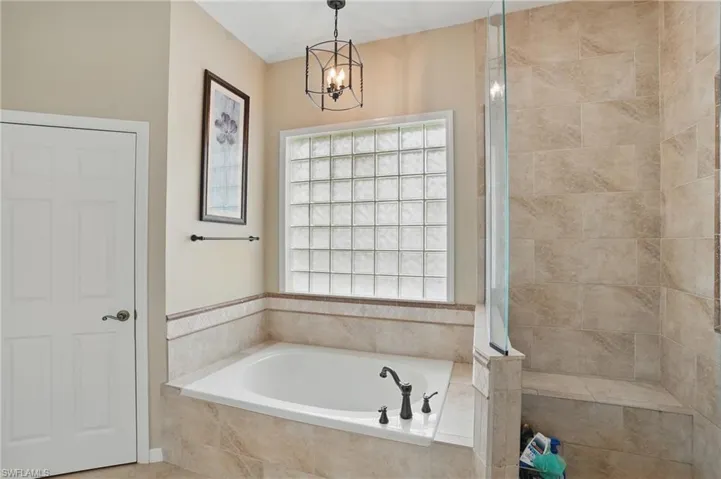 Full bathroom featuring a bath, a chandelier, and tiled shower