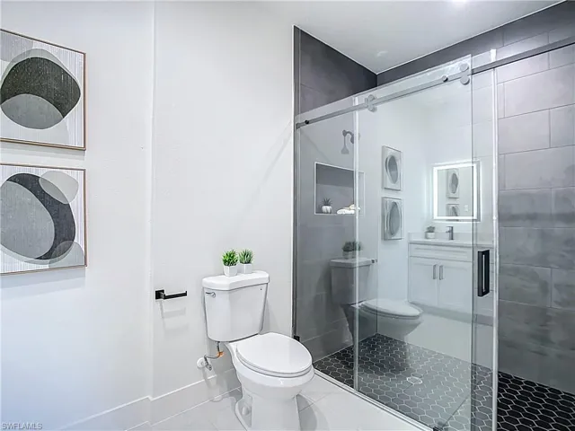 Contemporary bathroom featuring a frameless glass shower enclosure with a sliding door, dark hexagon tile shower flooring, and light gray subway tile walls