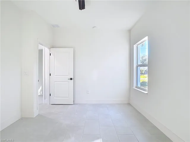 Bright room featuring light-colored tile flooring, white painted walls, a white paneled door with dark hardware, and a double-hung window with a white frame