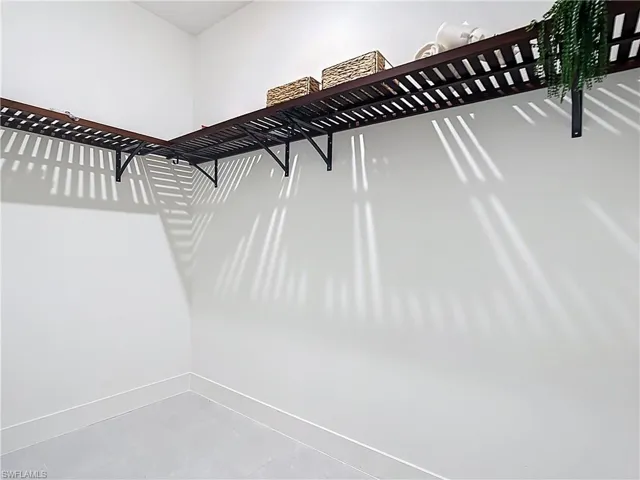 White-painted walls featuring L-shaped wood-slat shelving with black metal brackets and light gray tile flooring
